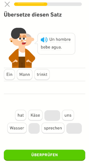 Screenshot einer Übung zum spanischen Satz „Como un tomate rojo“. Die deutschen Wortkacheln darunter ergeben den Satz „Ich esse eine rote Tomate“ und wiederum darunter befindet sich ein grünes Feld mit der Meldung „Überprüfen“.