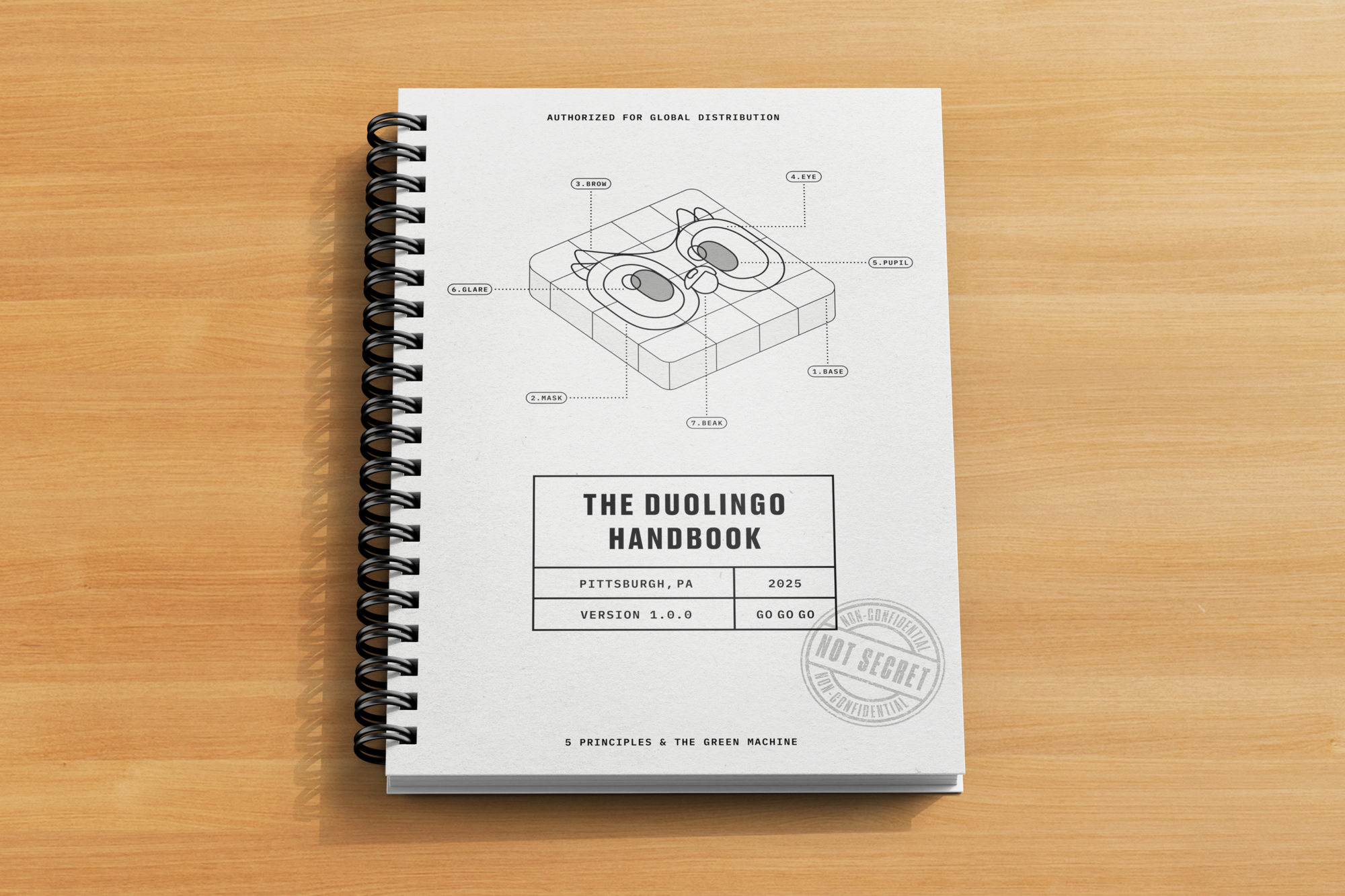 A spiral bound book with the title, "The Duolingo Handbook" and a diagram of the Duolingo app icon on its cover. 